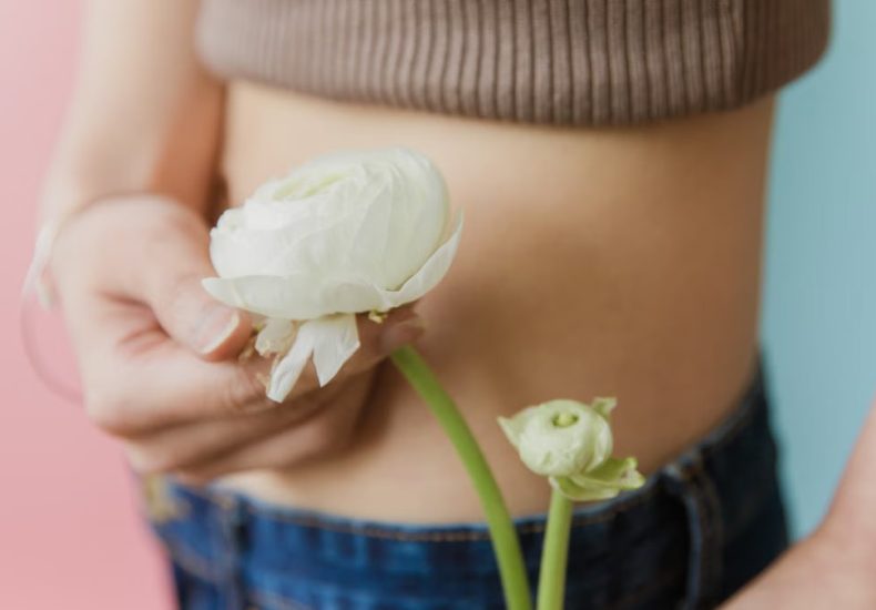 Delicate close-up of a woman's abdomen holding a white rose in hand